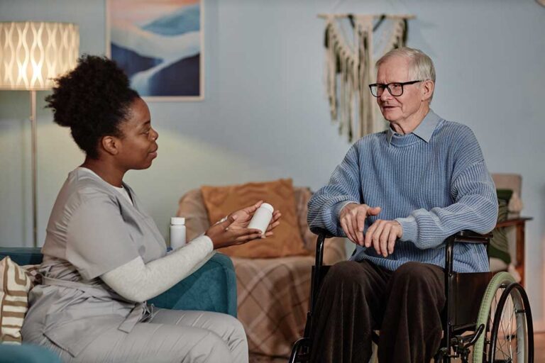 An older adult socializing with a caregiver in a sunlit, comfortable living room setting.